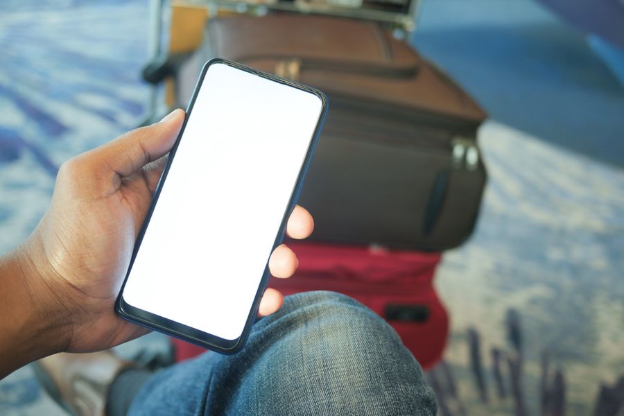 A person holding a smartphone in an airport with luggage visible, ideal for travel and tech concepts. — O Tele Agent: a página de suporte que responde de volta.