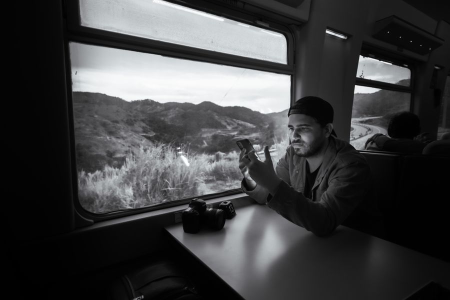 Man using a smartphone on a train journey through scenic landscape.