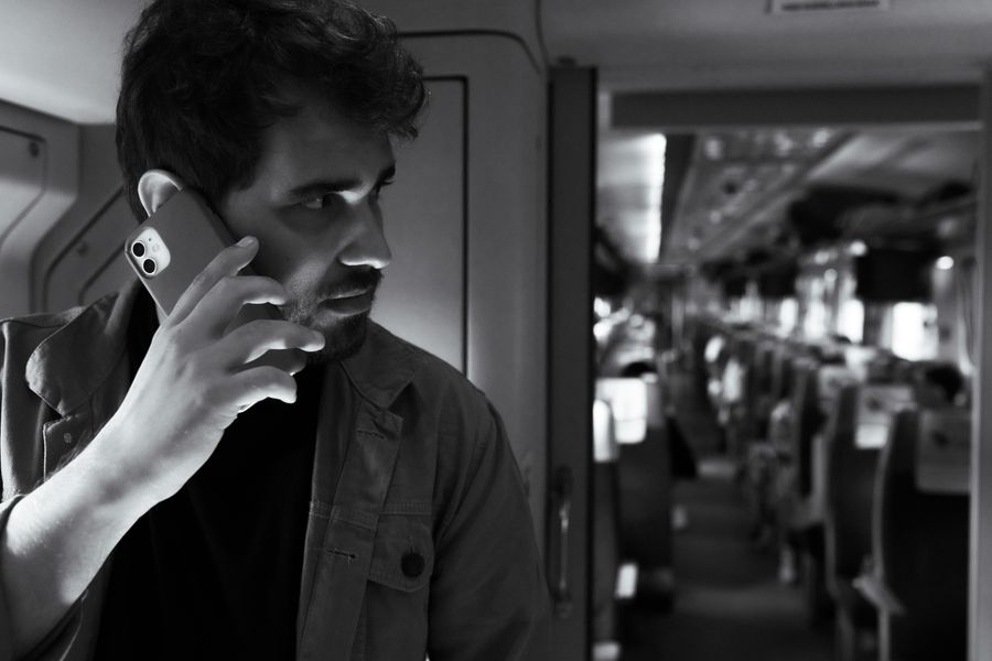 Black and white photo of a man using a smartphone while traveling on a modern train. — Café office: hotspot running, video call stable, no hotel Wi-Fi roulette.