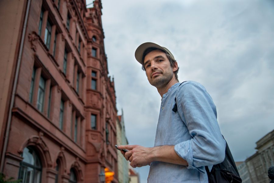 Casually dressed man using smartphone in Berlin city street with historic architecture. — Feiras noturnas e trens tardios — conectado o caminho todo.
