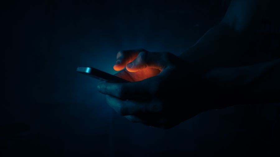 man holding a mobile phone in the dark — O skyline de Cabo Verde ao entardecer: videochamada para casa com a cidade inteira atrás.