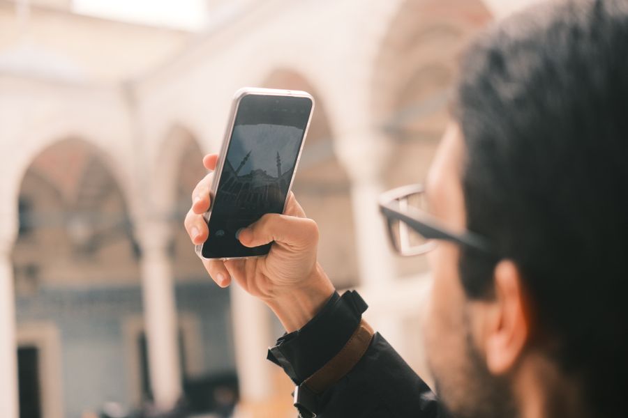 An adult male photographs a mosque using a smartphone outdoors with a focus on capturing architecture. — O expresso do aeroporto de São Tomé and Príncipe: passagem na carteira antes do avião pousar.