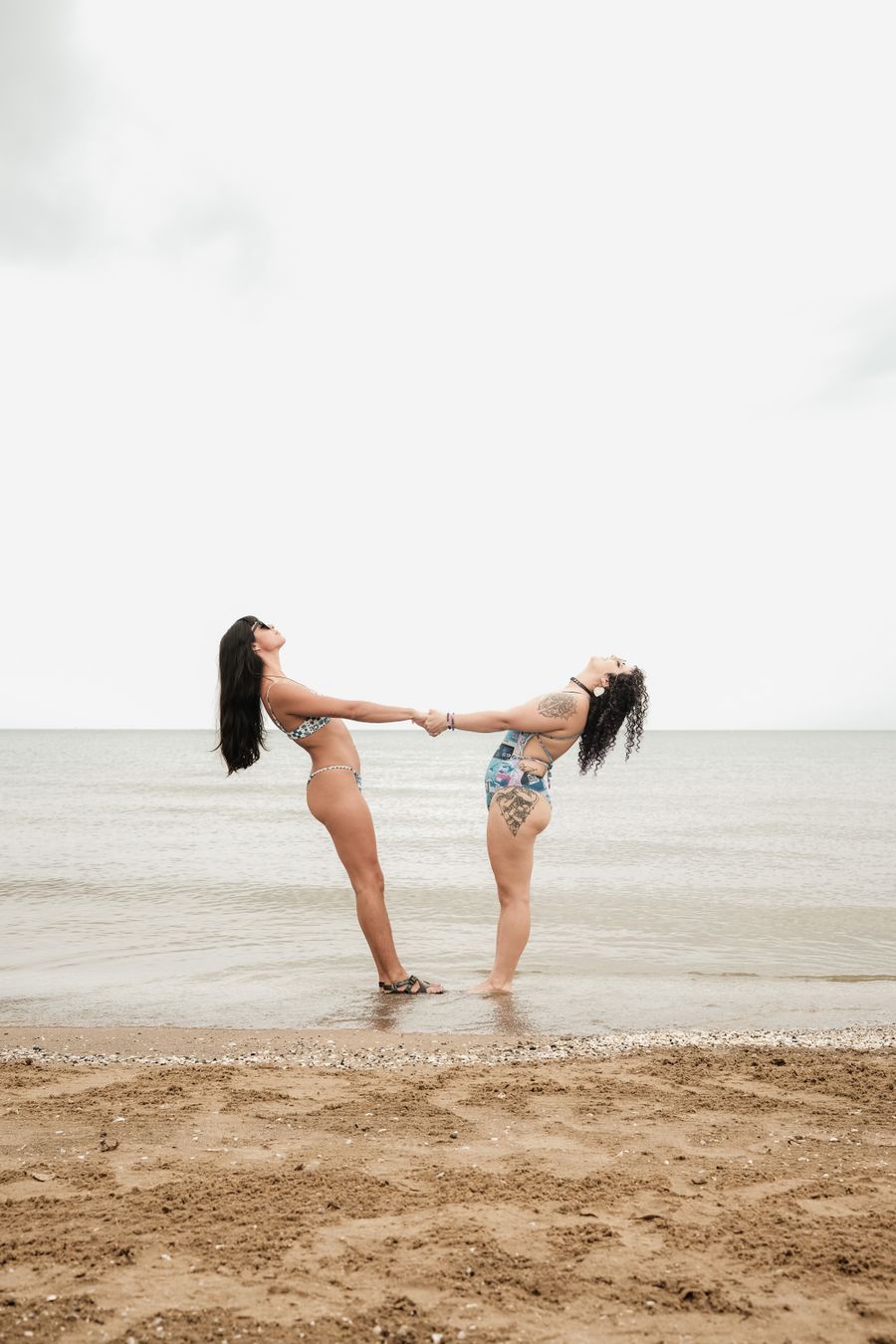 two women standing on the beach holding hands — Changelog: O crachá da conferência: ingresso QR escaneado, agenda sincronizada.