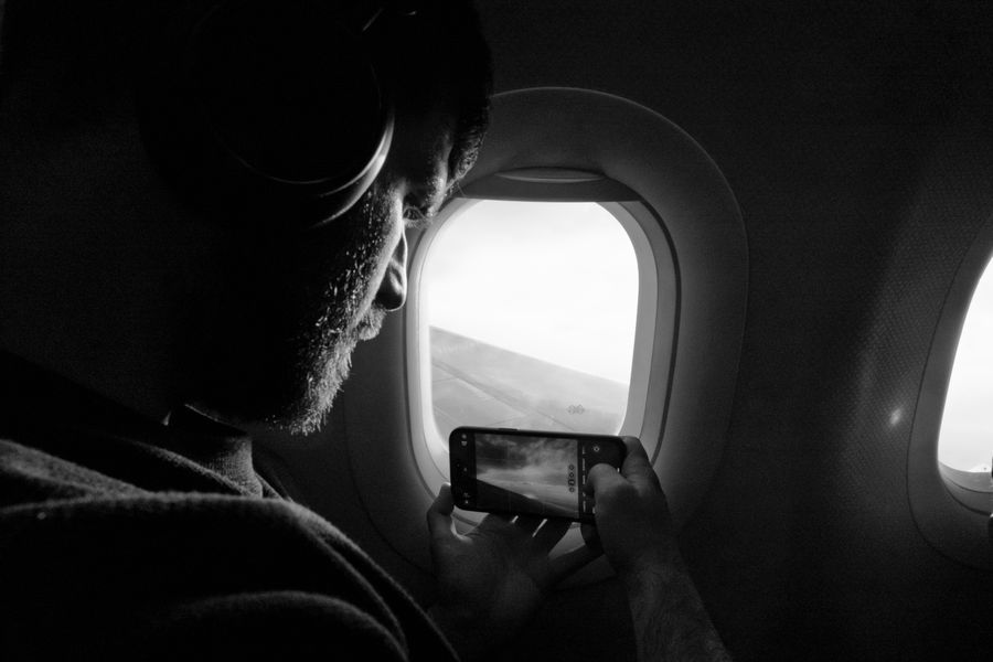 Man taking photo out of airplane window, capturing wing view with smartphone.