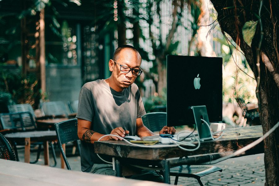 man working on computer at outdoor cafe — Pergunte no seu idioma — inglês, espanhol, francês, alemão, português, japonês.