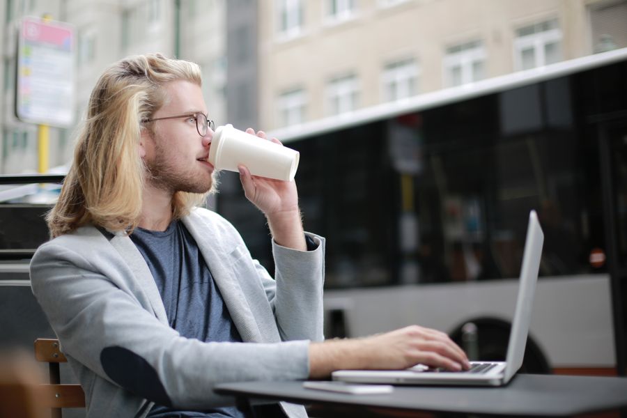 man drinking coffee while working on his laptop — Viagens reais, conectividade real — é para isso que o produto existe.