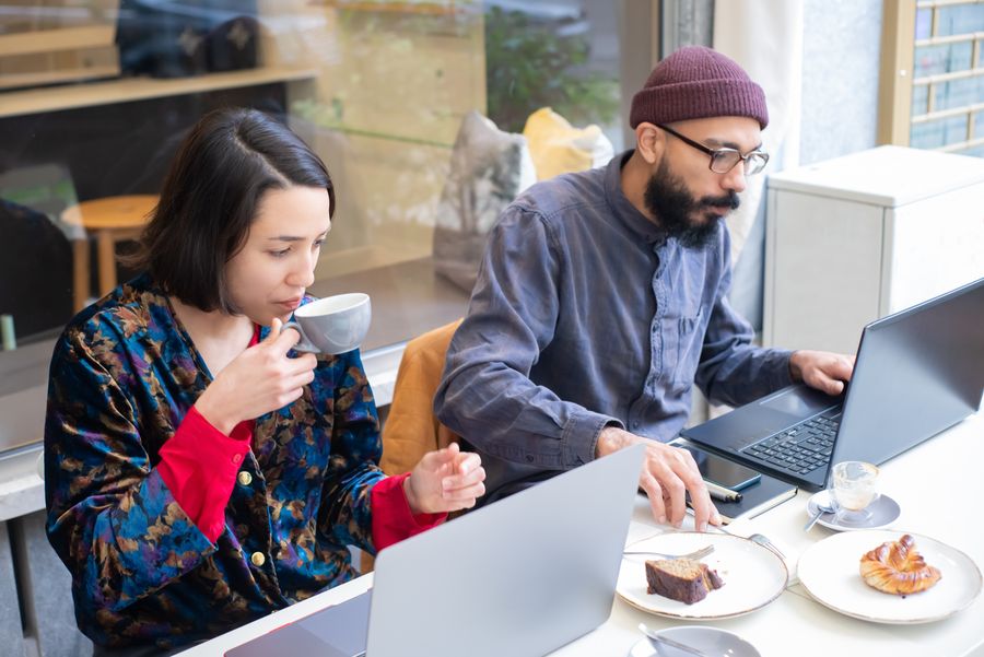 man and woman sitting in a cafe and using laptops while having a coffee and cake — O distrito financeiro de Mozambique: o hotspot sustenta a reunião inteira.