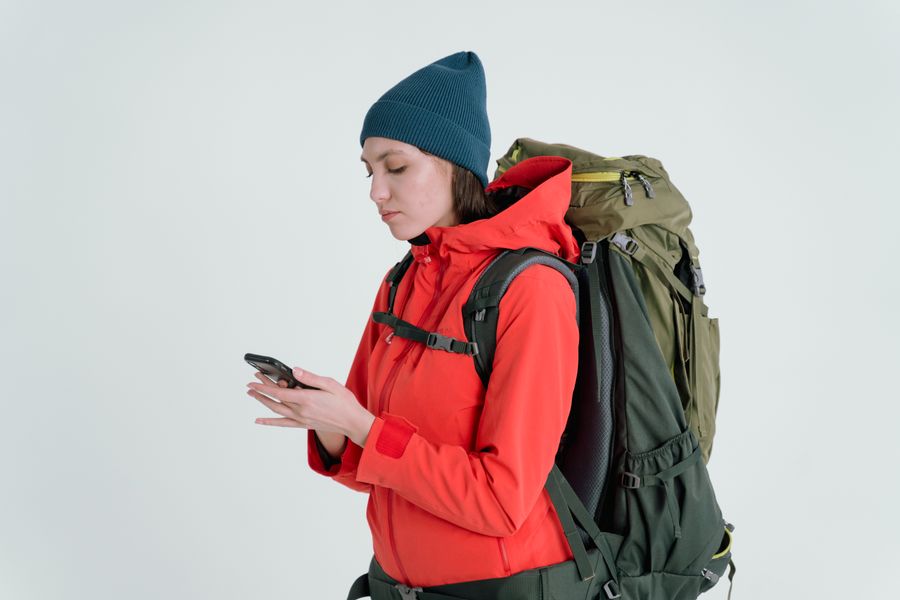 A woman in outdoor gear checking her smartphone, ready for adventure. — Dirigindo por Guinea-Bissau: o trânsito ao vivo desvia do engarrafamento.